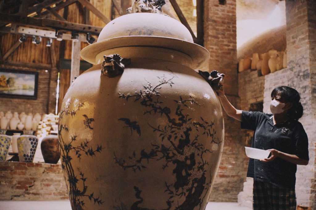 A skilled artisan works on a large ceramic vase in a traditional Vietnamese pottery workshop, showcasing intricate designs.